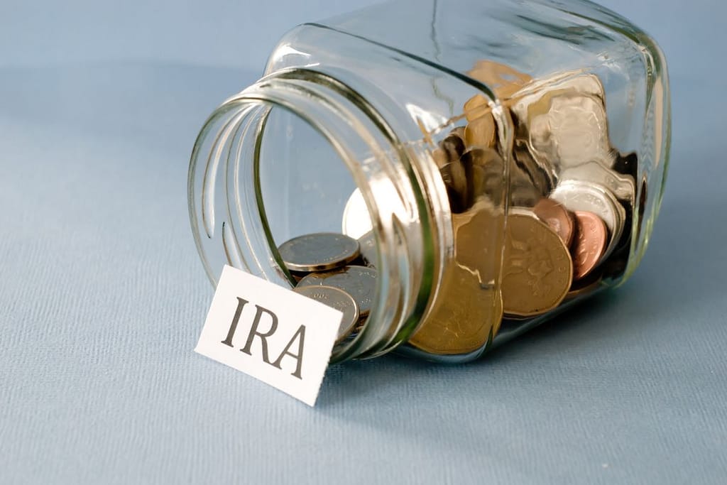 A glass jar containing coins and a sign indicating IRA, optimizing taxes with IRA contributions.