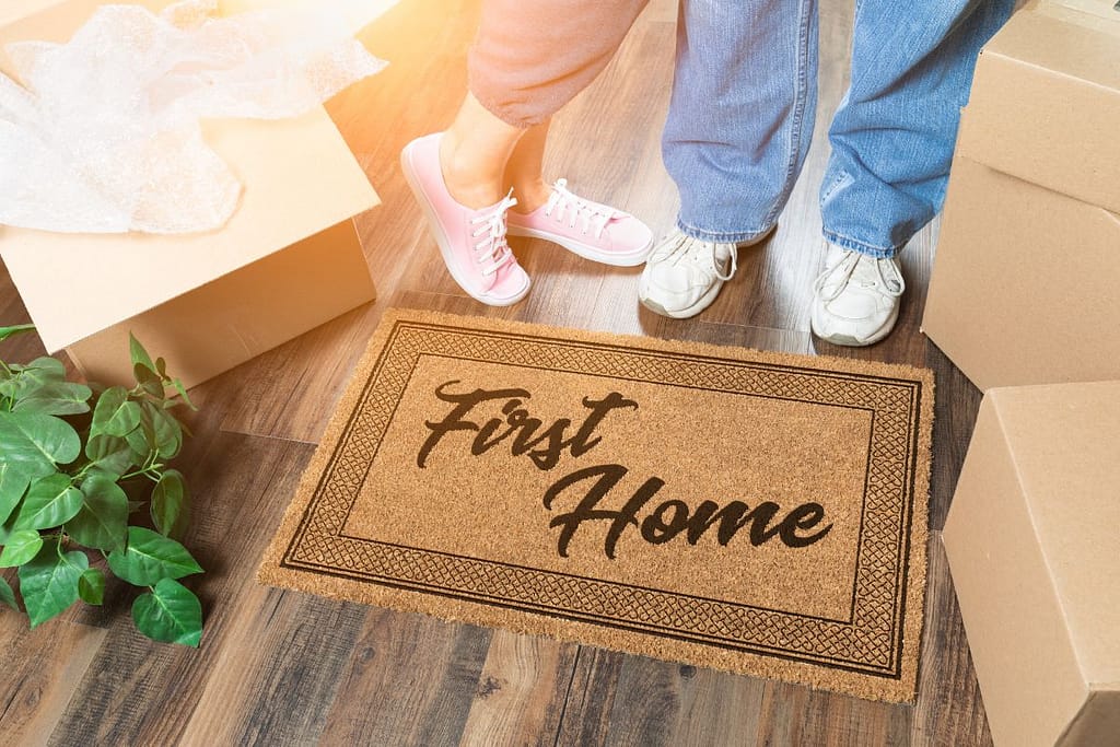 Two first-time home buyers standing next to a first home mat.