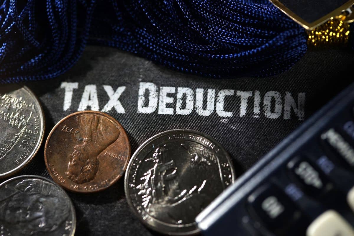 The word tax deduction is written on a piece of paper with coins and a calculator.