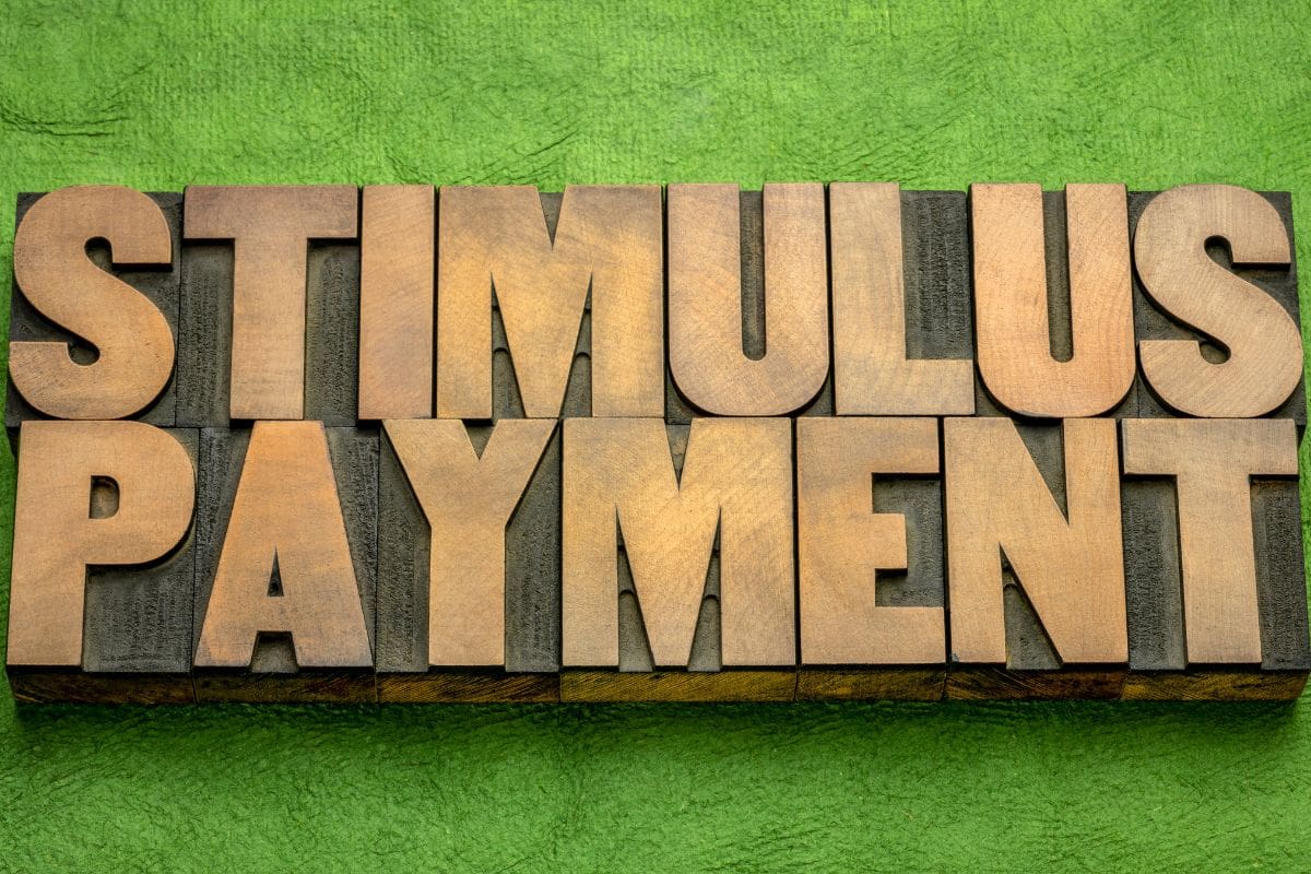 The word stimulus payment in wood type on a green background.
